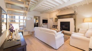 Ein geräumiges Wohnzimmer mit hoher Decke, Kamin, einer Couch, einem Fernseher und einem Essbereich.