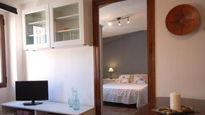 A room with a TV on a white cabinet, a mirror reflecting a bed with a patterned bedspread, and a wooden table with a candle and stones. - COZY APARTMENT 70 m. from THE BEACH in TOSSA (Tossa de Mar)