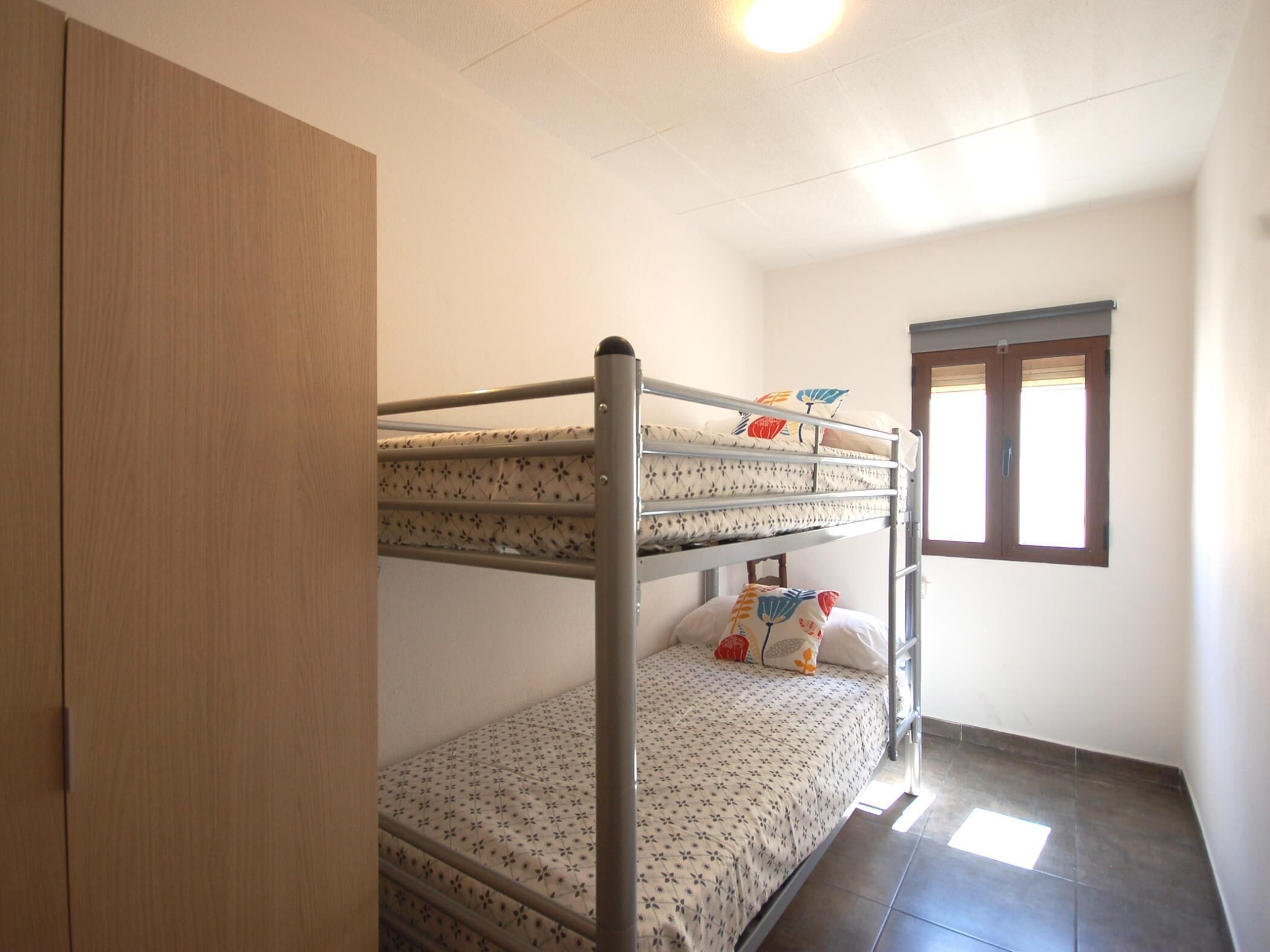 Habitación con literas, un armario, una ventana y suelo de baldosas.