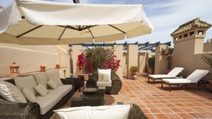 Un espace extérieur aménagé avec des meubles en osier, un parasol blanc et des plantes en pot.
