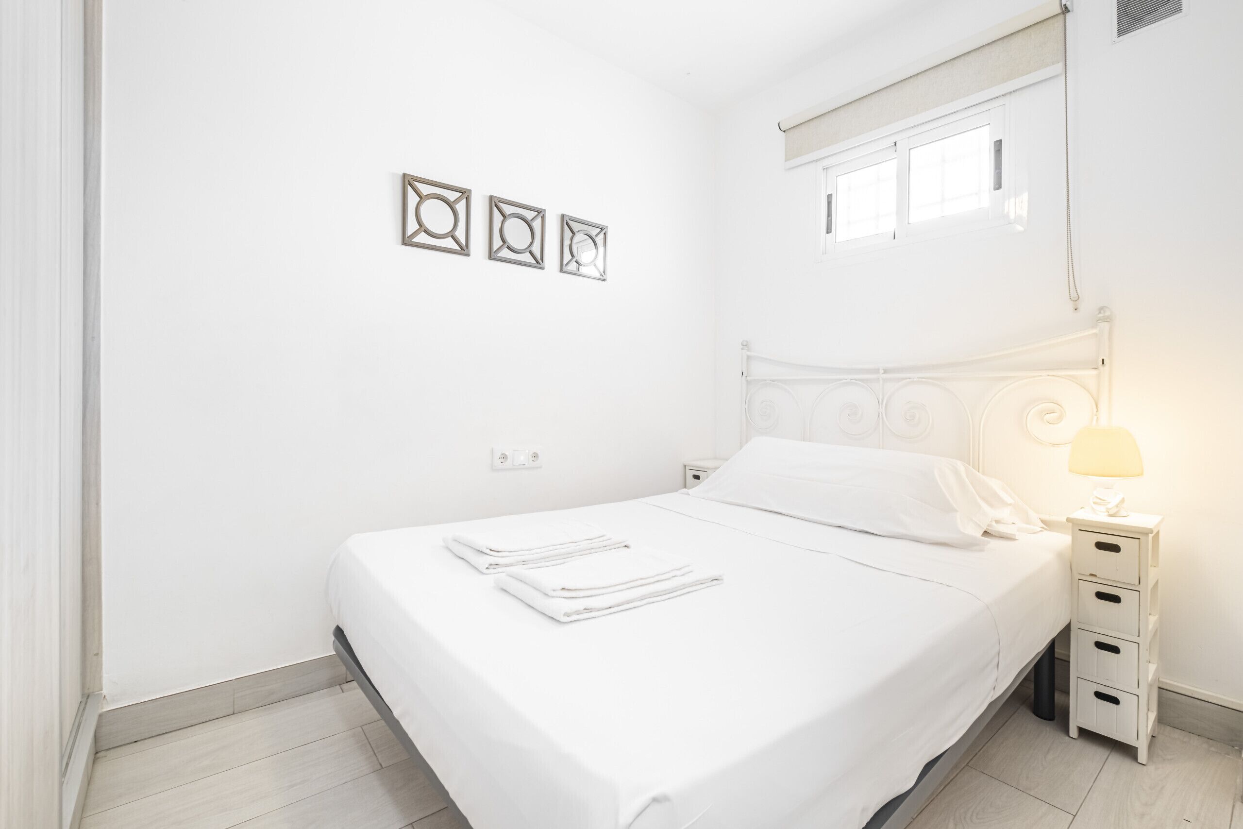 Un letto rifatto con lenzuola bianche, un comodino con una lampada e tre quadri appesi al muro.