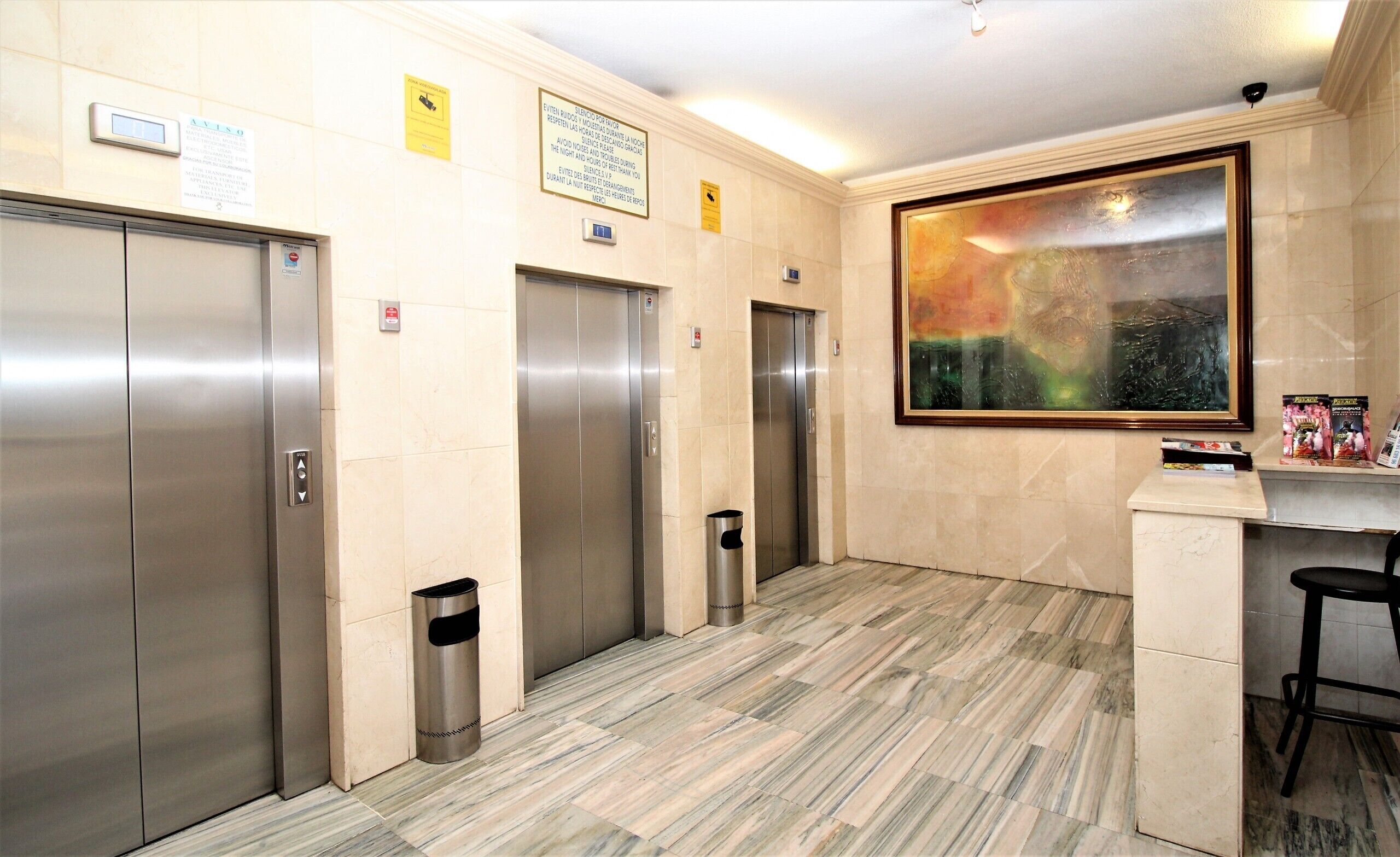 An elevator area with three elevators, a trash bin, and a framed abstract painting on the wall.