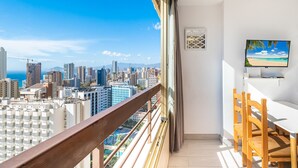 A balcony with a city view, a dining area with wooden chairs, and a flat-screen TV on the wall. - Acuarium 3-19-E (Benidorm)