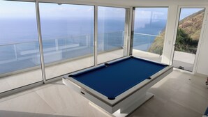 A pool table in a room with large windows overlooking a coastal landscape. - Quinta Pereira ... beautiful panoramic views and ocean sunsets  (Faja Da Ovelha)