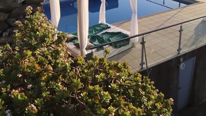 A modern infinity pool with a glass balustrade overlooking the sea, a stone wall, and a bed with a green cover. - Quinta Pereira ... beautiful panoramic views and ocean sunsets  (Faja Da Ovelha)