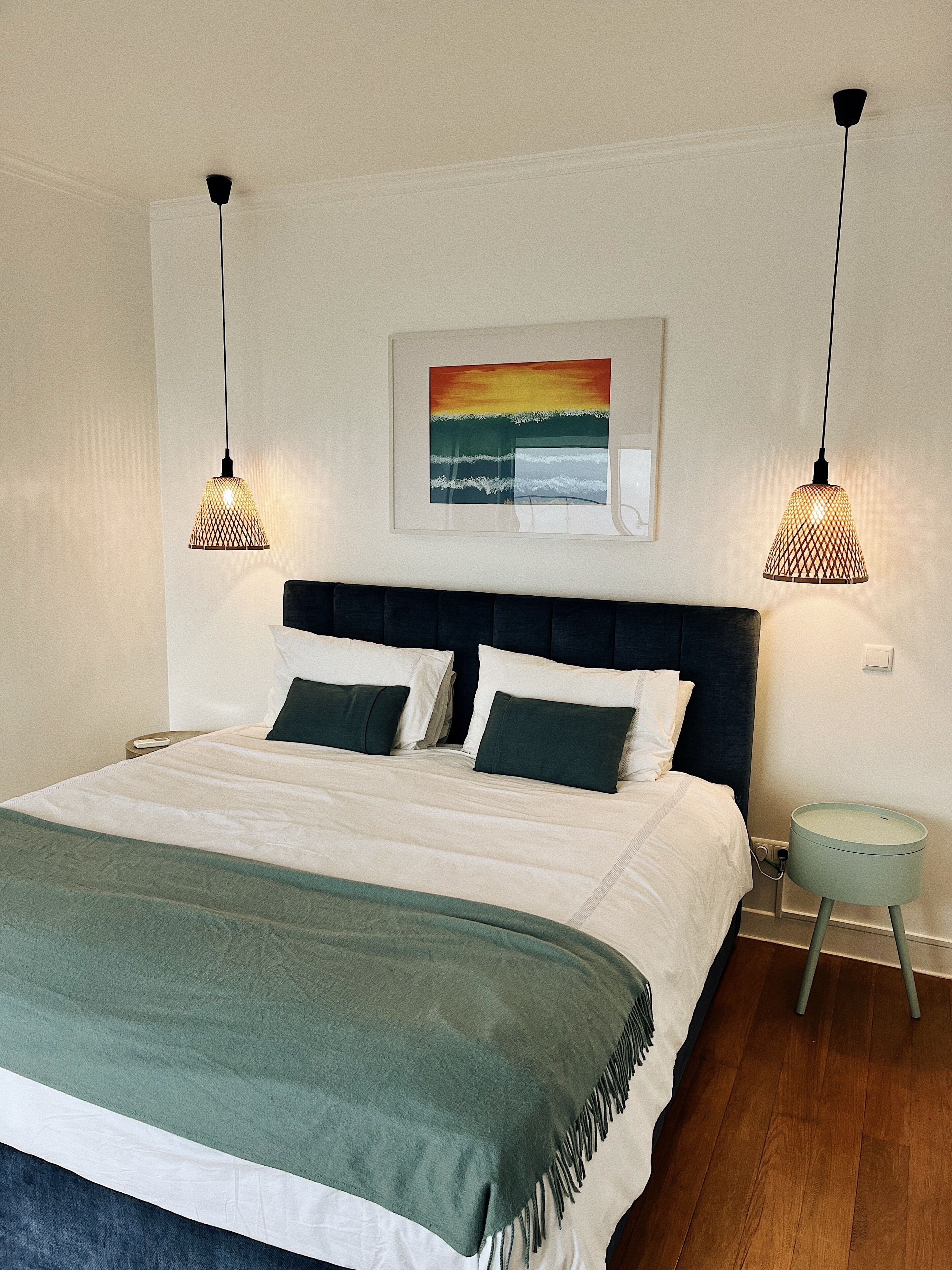 A neatly made bed with a green throw, two bedside lamps, a nightstand, and a framed picture on the wall.