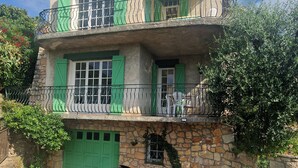 Ein zweistöckiges Steinhaus mit grünen Fensterläden und einem weißen Auto vor der Tür.