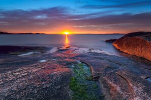 A rocky shoreline at sunset with a calm sea and distant land.