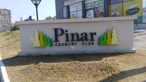 Señal de Pinar Country Club con un edificio moderno al fondo.