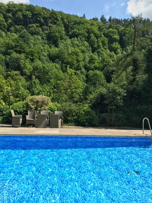 A swimming pool with a clear blue water surface, surrounded by a patio area with wicker furniture. - Riversdale Lodge is set in the heart of Symonds Yat overlooking the River Wye. (Symonds Yat)