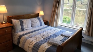 A bedroom with a wooden bed, striped bedding, two bedside lamps, a nightstand with a drawer, and a window with curtains. - Riversdale Lodge is set in the heart of Symonds Yat overlooking the River Wye.  (Symonds Yat)