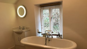 A bathroom with a freestanding bathtub, a round mirror with lights, a sink, and a window with blinds. - Riversdale Lodge is set in the heart of Symonds Yat overlooking the River Wye.  (Symonds Yat)