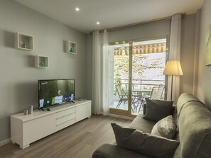 A modern living room with a flat-screen TV on a white console, a grey sofa with cushions, and a balcony with a table and chairs. - POOL APARTMENT NEAR BEACH 3 (Tossa de Mar)