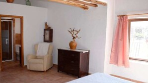 A bedroom with a bed, a chair, a dresser, a vase, and a window with curtains. - CAN PERE Authentic country house with a pool, just 6 km from the nearest beach (Sant Joan de Labritja)