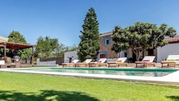 A pool area with lounge chairs, a pergola, and a building with a stone facade. - CAN PERE Authentic country house with a pool, just 6 km from the nearest beach (Sant Joan de Labritja)