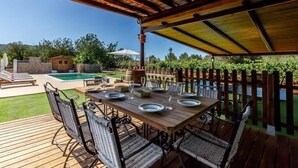 An outdoor dining area with a wooden table set for four, surrounded by wicker chairs, under a wooden pergola with a hanging light fixture. - CAN PERE Authentic country house with a pool, just 6 km from the nearest beach (Sant Joan de Labritja)
