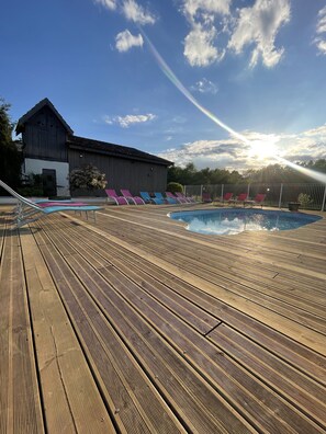 Une terrasse en bois avec une piscine, des chaises longues et un bâtiment en arrière-plan.