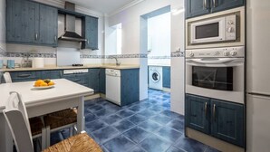 Una cucina compatta con mobili azzurri, un piano di lavoro bianco, forno integrato e lavatrice.