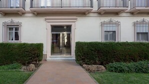 Ingresso di un edificio con vialetto lastricato, porte in vetro e una piccola tettoia sopra l'ingresso.
