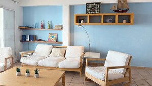 Een woonkamer met een bank, stoelen, een salontafel en planken met decoratieve objecten.