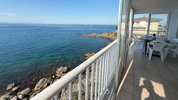 Een balkon met uitzicht op zee, een tafel met stoelen en een potplant.