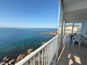 Een balkon met uitzicht op zee, een tafel met stoelen en een potplant.