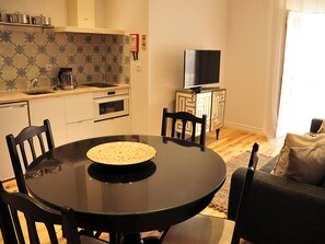 A compact kitchen with a dining area. It includes a stove, oven, sink, and a small cabinet with a TV.