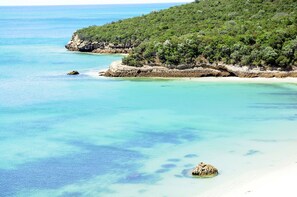A coastal landscape with clear turquoise waters, a sandy beach, and a forested hill. - Fully equipped air-conditioned apartment in central Setúbal (Setúbal)