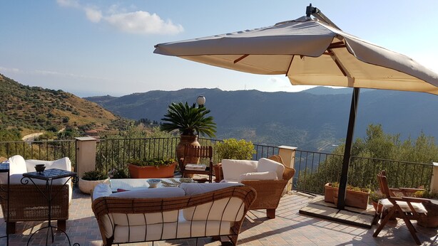 A terrace with wicker furniture, a large umbrella, and potted plants. - Apartment in two-room villa called Lipari 4/5 beds (Reitano)