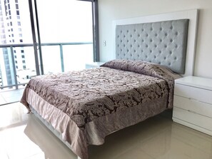 Ein modernes Schlafzimmer mit einem großen Bett, einem gepolsterten Kopfteil und Blick auf eine Stadtkulisse durch große Fenster.