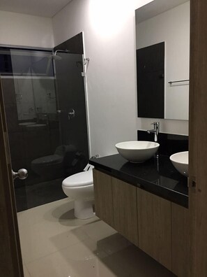Ein modernes Badezimmer mit einer Glasdusche, einer weißen Toilette und zwei Waschbecken mit schwarzen Arbeitsplatten.