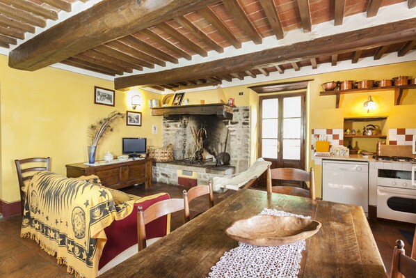 A rustic kitchen with a stone fireplace, wooden beams, and a dining area with a wooden table and chairs.