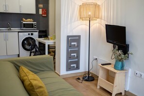 Une chambre d’hôtel compacte comprenant un lit, un bureau avec un micro-ondes, un lave-linge, une télévision et une lampe.