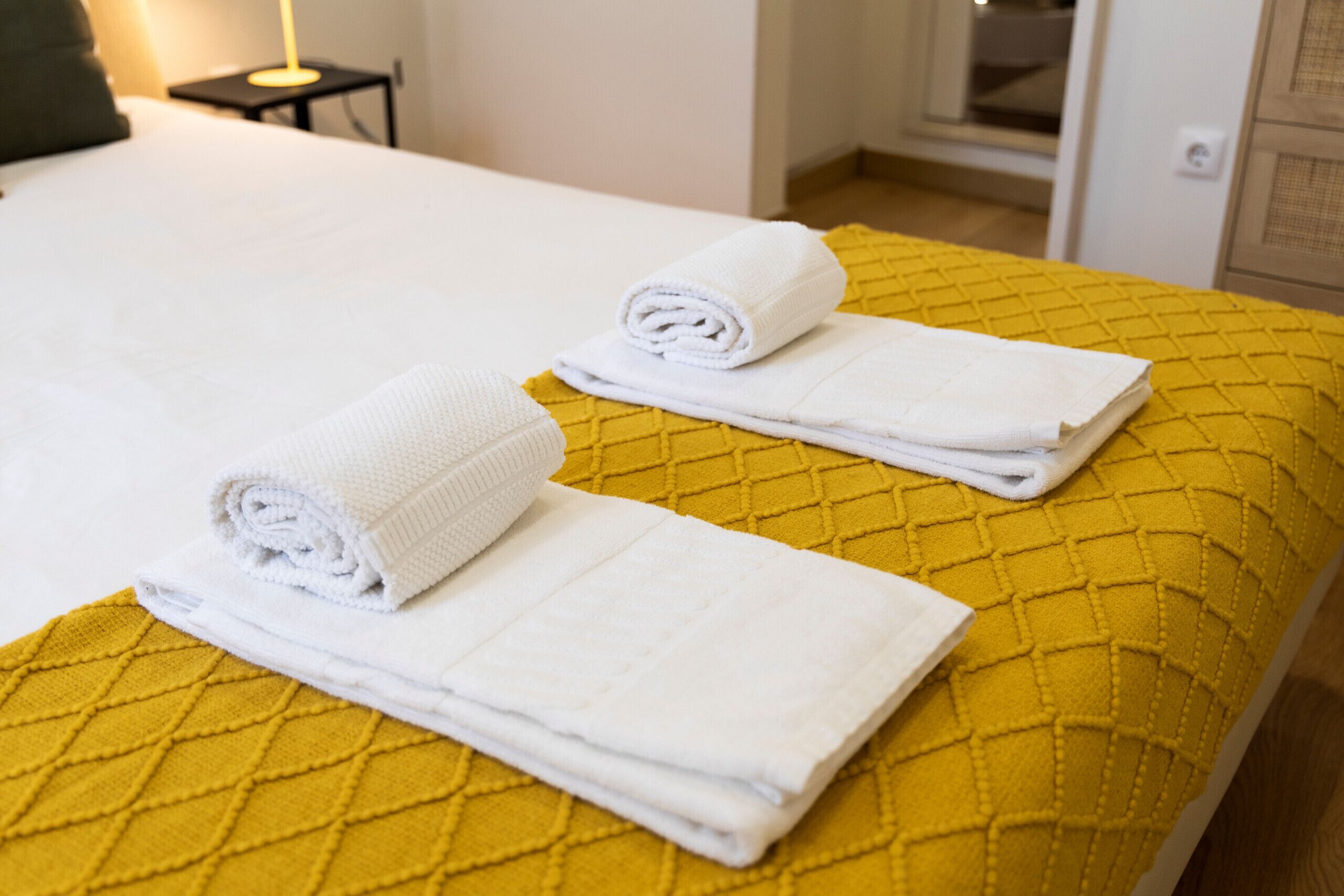 A bed with a yellow quilted bedspread and two neatly folded white towels.