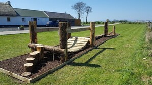 Een houten hindernisbaan met boomstammen en een helling in een grasveld.