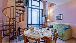 Ein Essbereich mit Wendeltreppe, einem für zwei gedeckten Tisch und einem grünen Sofa.