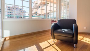 A room with a large window, a black leather chair, wooden flooring, and a view of buildings outside. - Cascais Park (Cascais)