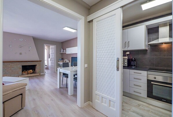 A modern kitchen with stainless steel appliances, a dining area with a white table and chairs, and a fireplace.