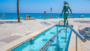 Una piscina con una estatua, un camino empedrado y el océano al fondo.
