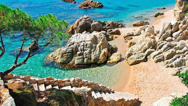 Un paisaje costero con aguas turquesas cristalinas, formaciones rocosas y una playa de arena.