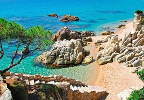 A coastal landscape with clear turquoise waters, rocky formations, and a sandy beach.
