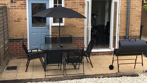A patio with a table and chairs, a barbecue grill, and a blue door. - Peaceful Retreat, Sovereign Harbour, Eastbourne - FREE WELCOME PACK (Eastbourne)