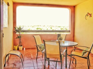 Een terras met een ronde tafel en vier stoelen, een bloempot en een uitzicht op een stadsbeeld door een raam.