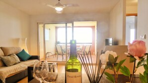 Een woonkamer met een bank, twee wijnglazen, een fles wijn en een vaas met een bloem.