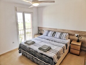Una camera da letto con un letto, un comodino, una ventola a soffitto e vista attraverso una porta scorrevole.
