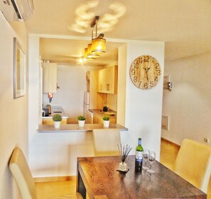 Un'area pranzo con un tavolo di legno, sedie, un orologio a muro e una cucina sullo sfondo.