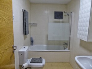 Een compacte badkamer met toilet, bad en wastafel.
