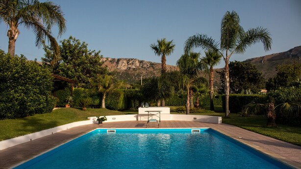 Una piscina rettangolare con un solarium bianco e un tavolo al centro.