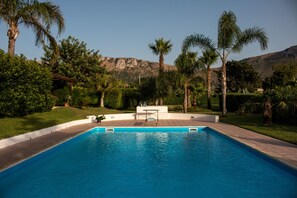 A rectangular swimming pool with a white deck and a table in the center. - Relaxing at Villa Maria (Terrasini)