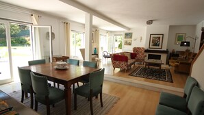 A spacious living room with a wooden dining table, green upholstered chairs, a red sofa, and a fireplace. - Cascais Downtown, Villa With Pool and Garden (Cascais)